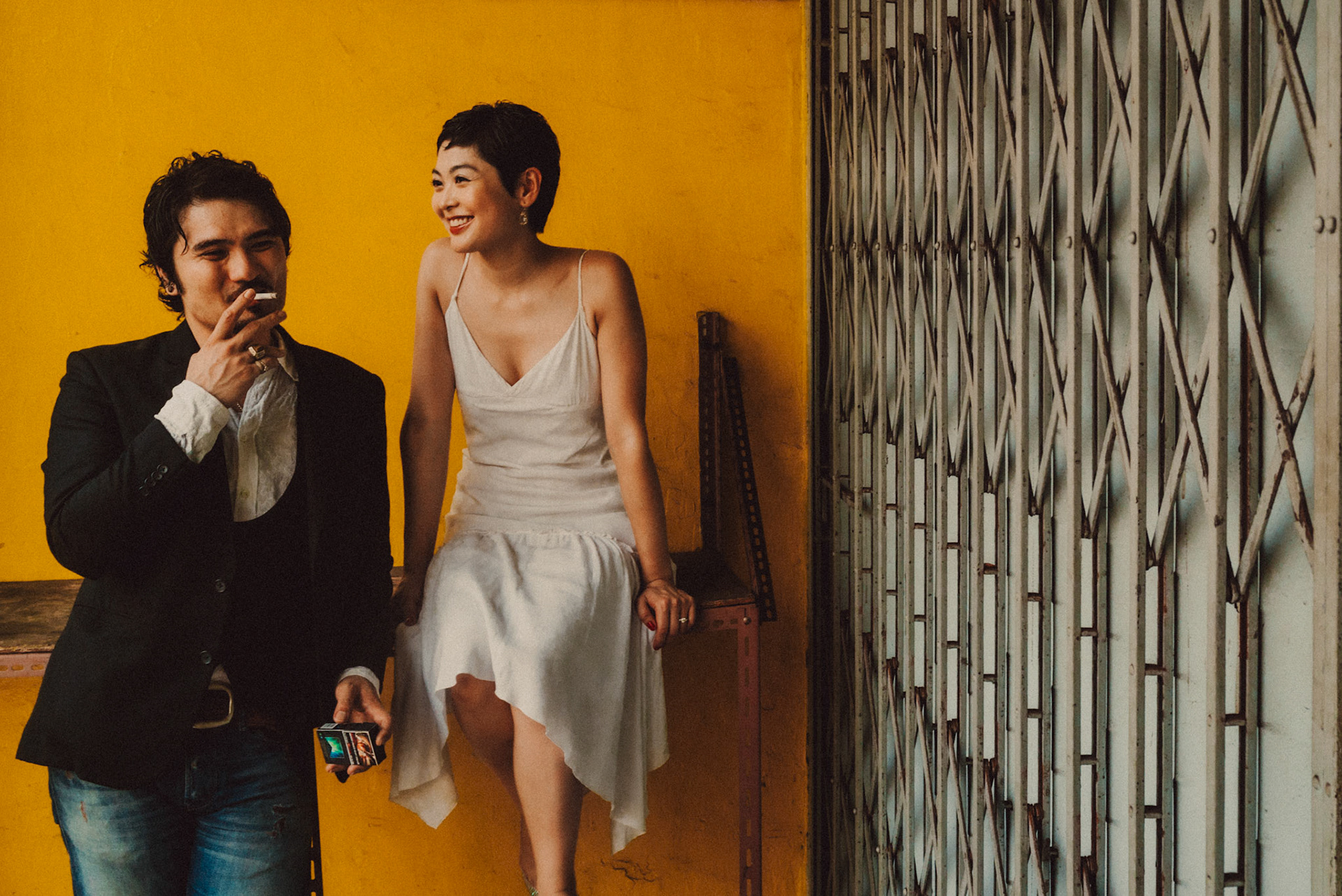 A Japanese couple in front of a bright yellow wall, from Ibuki and Emi's casual chill engagement shoot, Little India, Singapore, October 2015, Sony A7S.