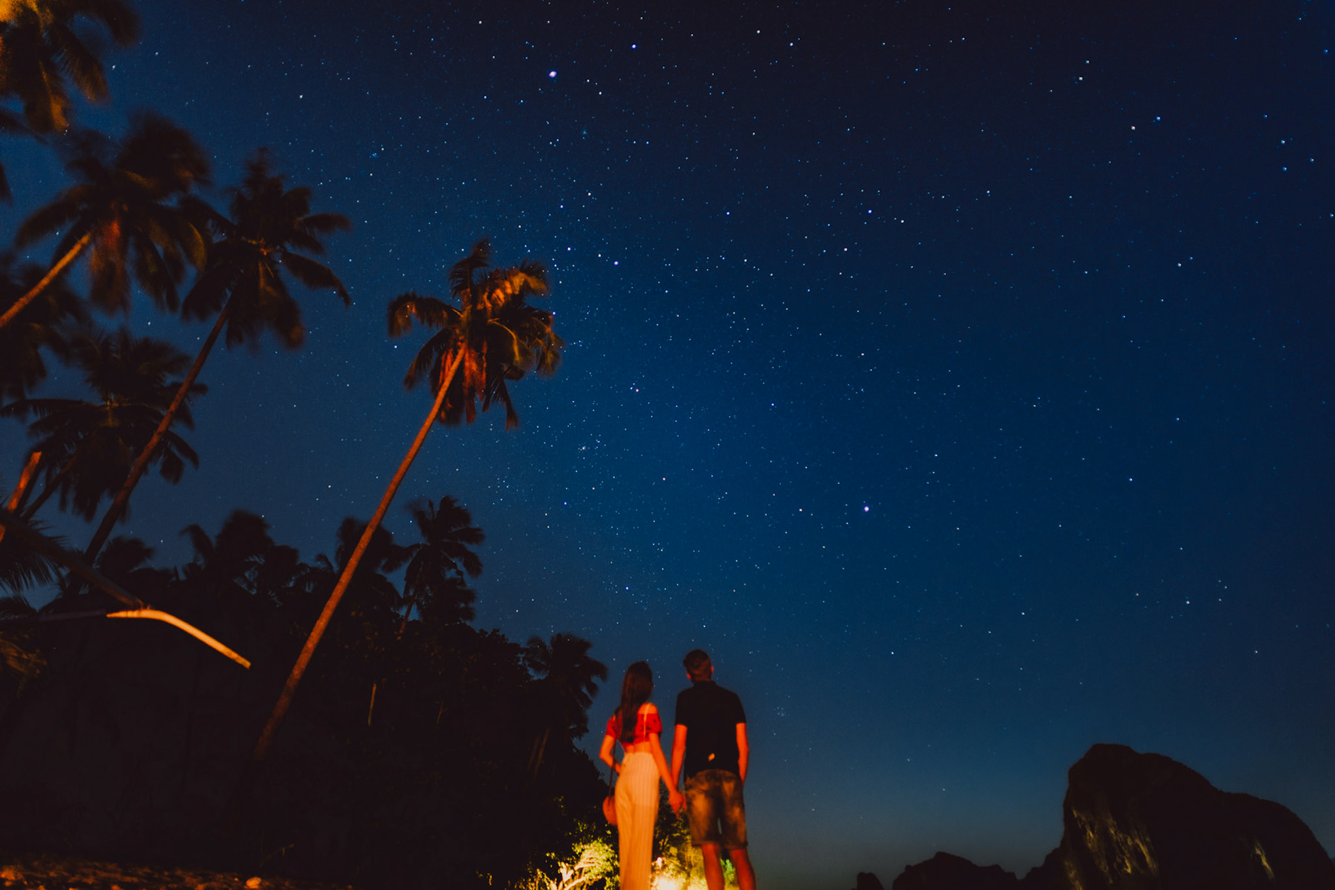 A starry night sky in Las Cabanas Beach with a couple beside a bonfire, El Nido, Palawan, Philippines, Southeast Asia, February 2019, Sony A7III.