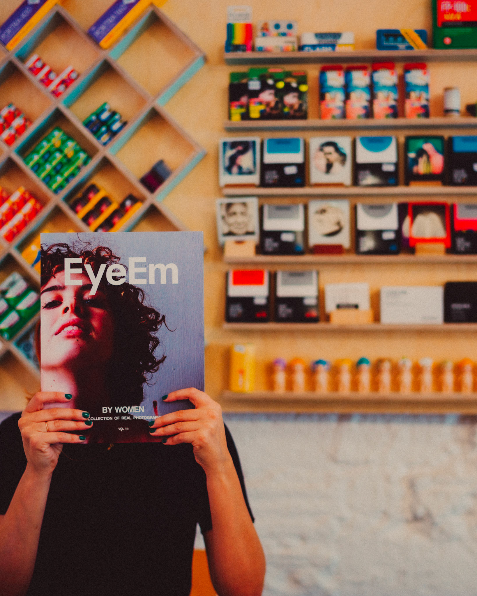 A woman in a film camera store holding a copy of EyeEm Magazine, Chandal, Barcelona, Spain, July 2016, Leica M.