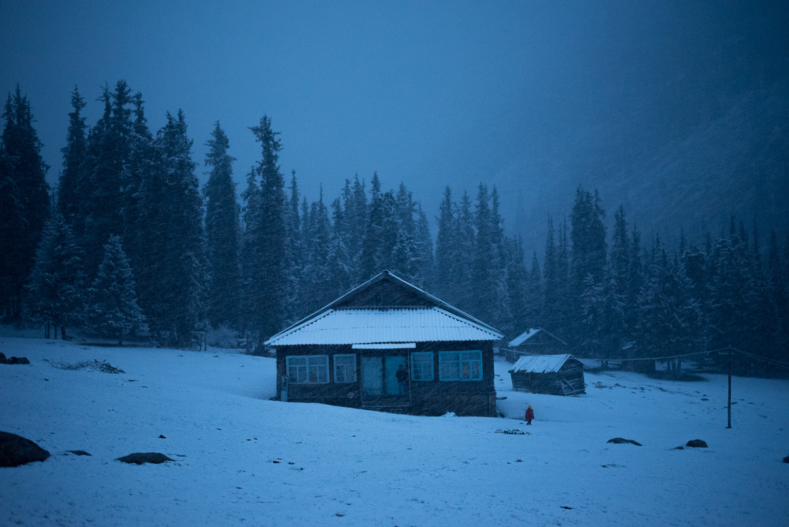 Chong, 18 h 04 – L’après-midi présageait l’installation définitive du printemps. Ce soir, le climat en a décidé autrement et transforme les montagnes vertes en paysage hivernal. De longues silhouettes noires viennent trancher un ciel caractéristique de l’heure bleue, tandis que la neige fraiche révèle une clarté irréelle.