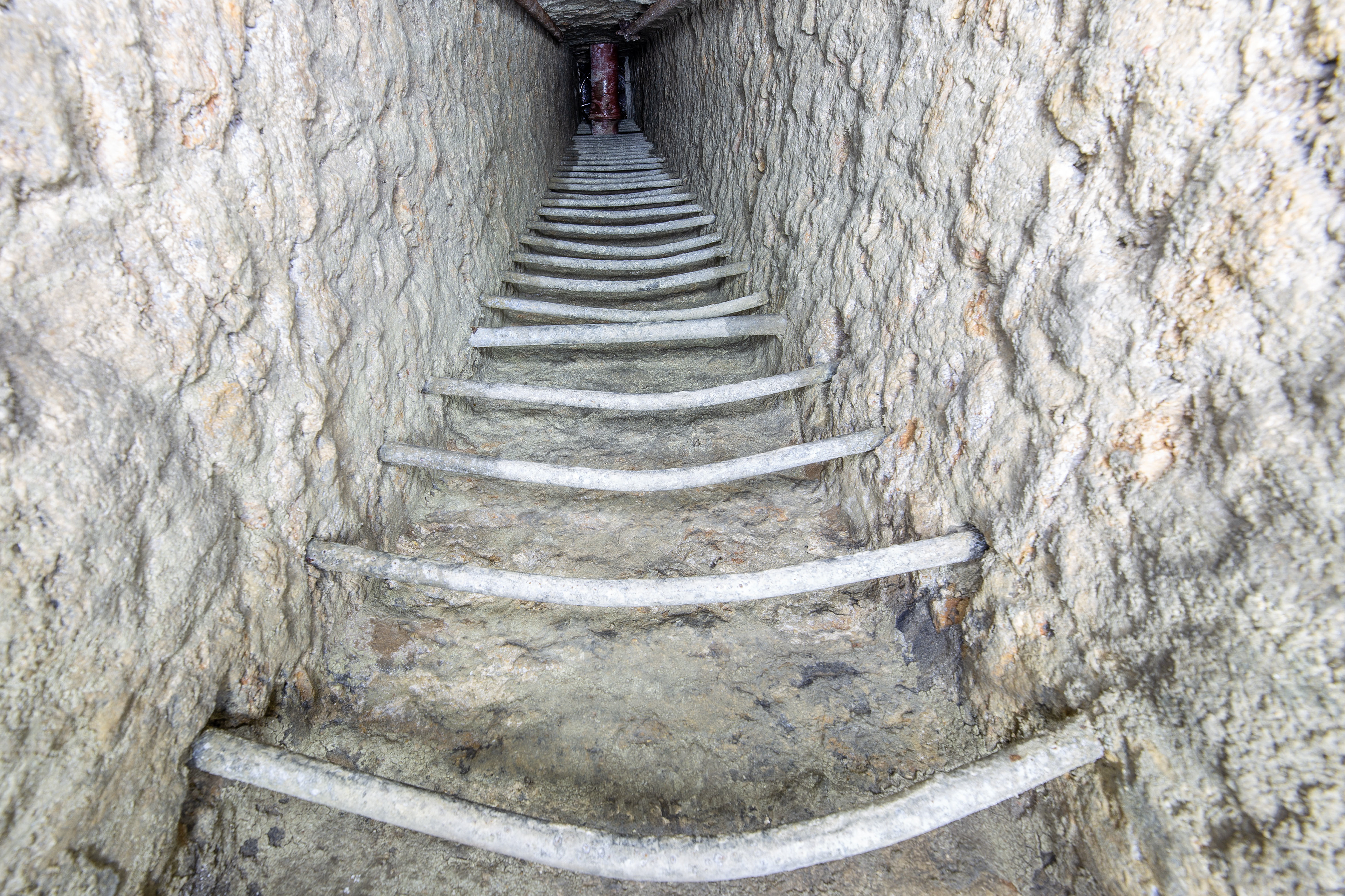Puits à barreaux encastrés. Un conduit de gaz traverse le puits et ne facilite pas sa descente.