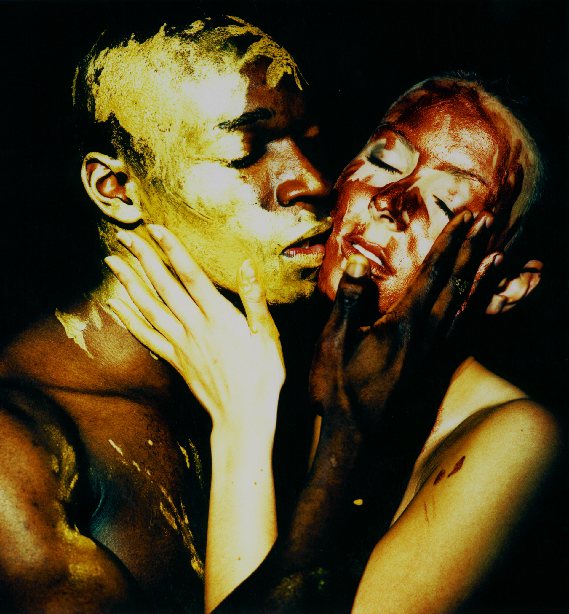 Jovan and Tina cheek to cheek smearing gold and copper paint on each other faces