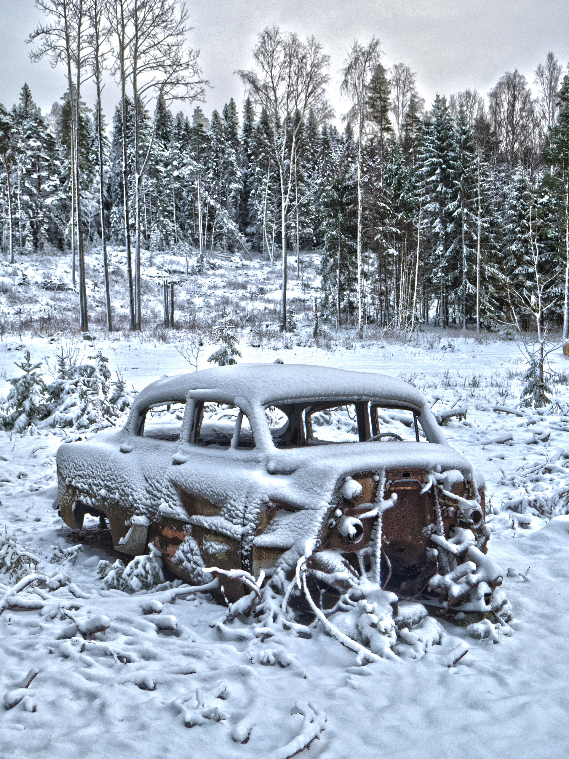 Snow covered old vintage rusty chevrolet with front missing abandoned in the field in winter