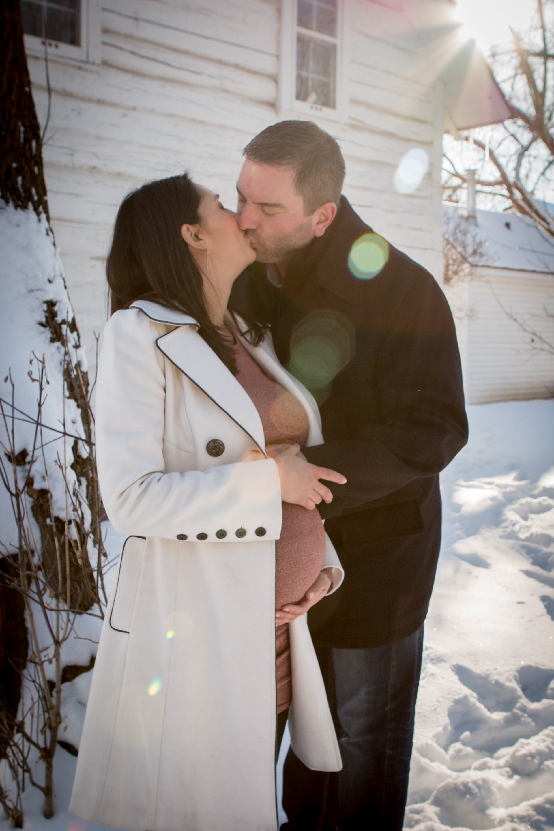 husband kissing pregnant wife in the snow