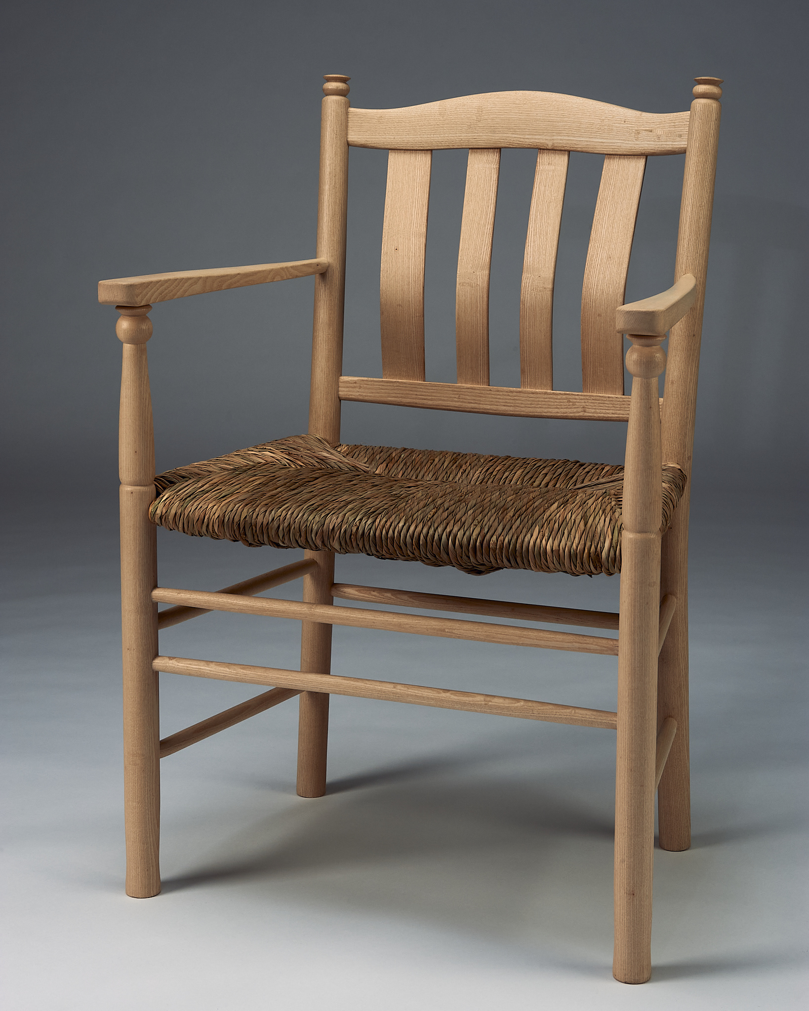 photo of a chair made of ash, a light-coloured wood, with a natural rush seat, posed at an angle, made by angus richardson