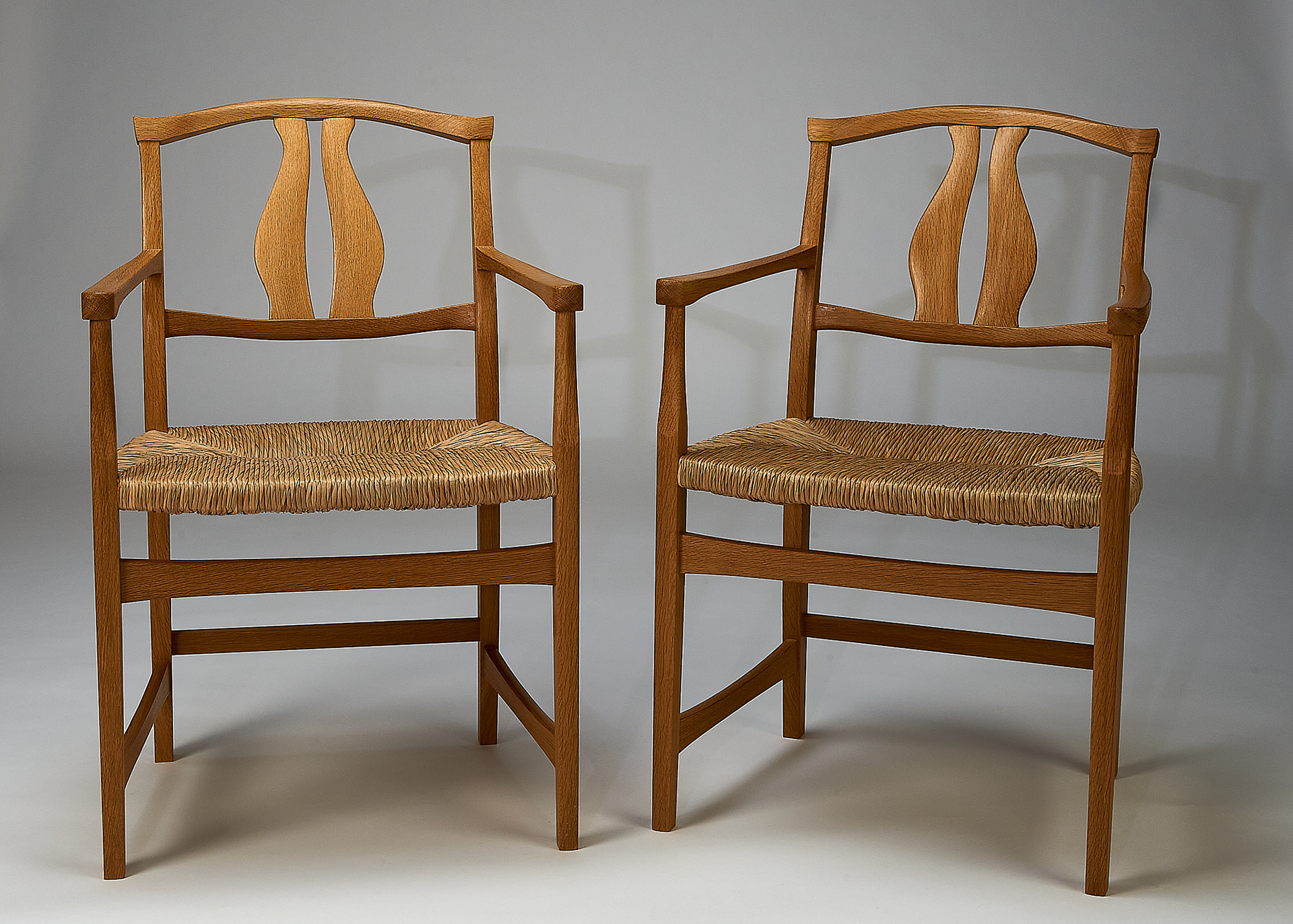 a pair of chairs made of oak with a beeswax finish, a rich, tan wood with natural rush seats, facing slightly towards eachother