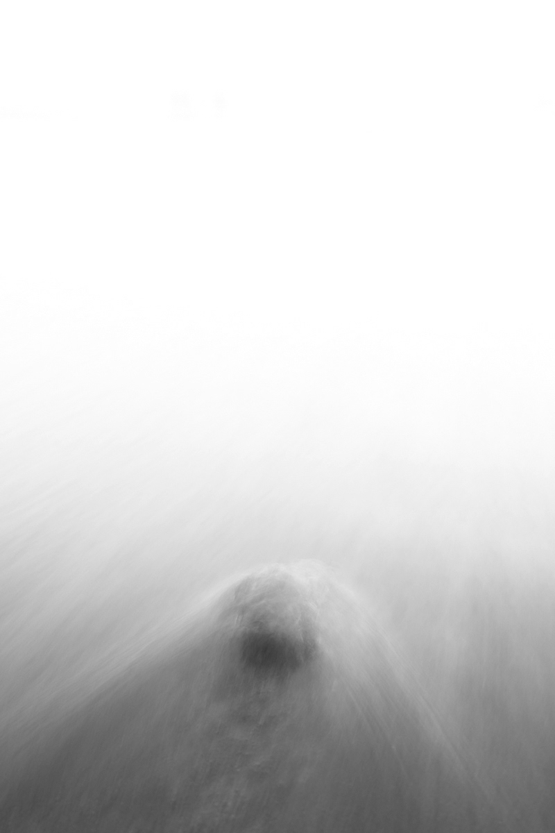 Imagen de larga exposición y minimalist de una roca en una playa con una ola rompiendo ilustrando un artículo sobre el punto en composición fotográfica