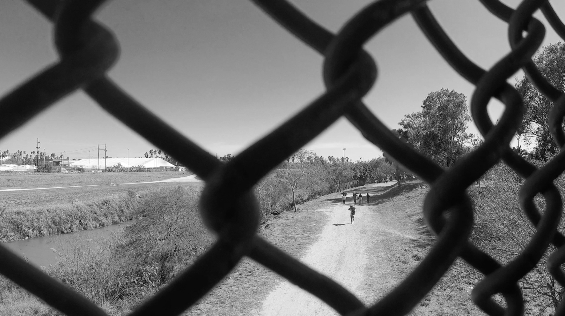 Looking east at the Rio Grande from the Gateway International Bridge connecting Brownsville, TX and Matamoros, MX. The Brownsville CBP tent court is on the left. The Matamoros asylum seeker camp is on the right.