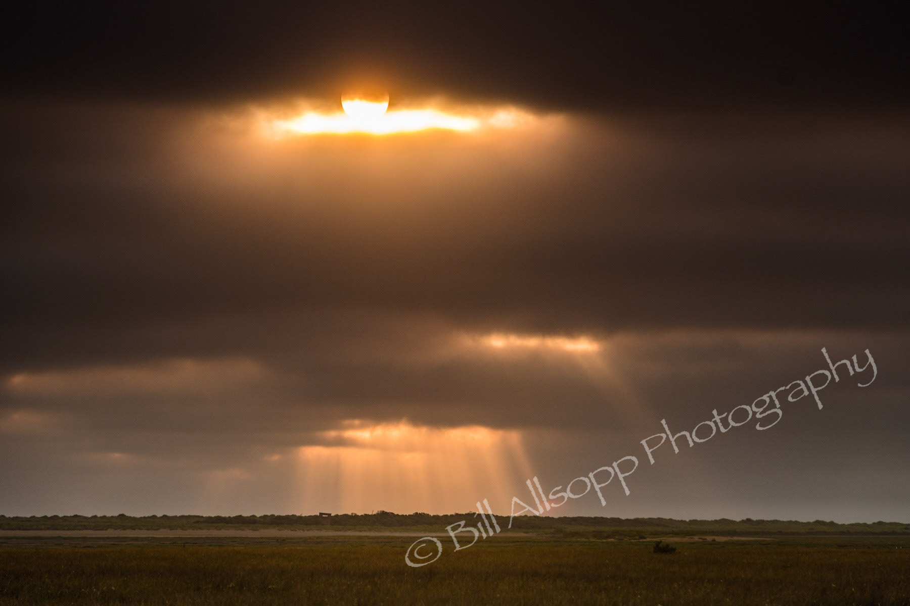 Crepuscular rays form over the marshes at Thornham, Norfolk at sunrise.