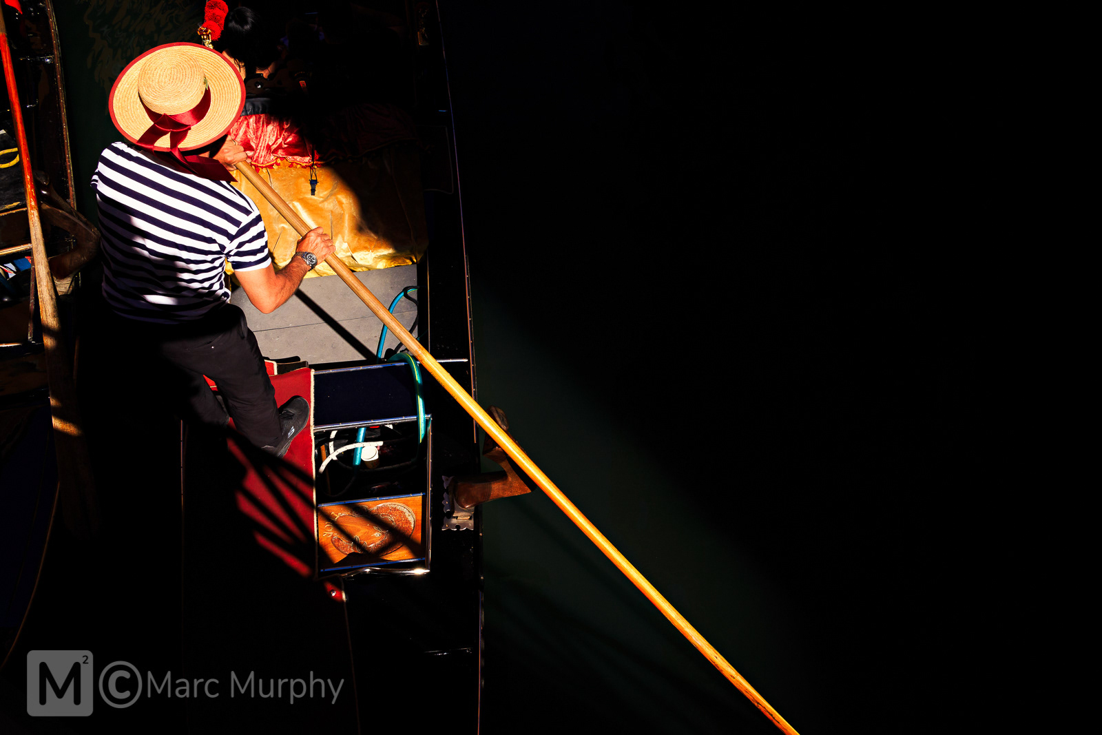 Overhead View of Venice Italy Gondolier Wearing Black and White Striped Shirt and Hat with Red Ribbon Rowing Gondola