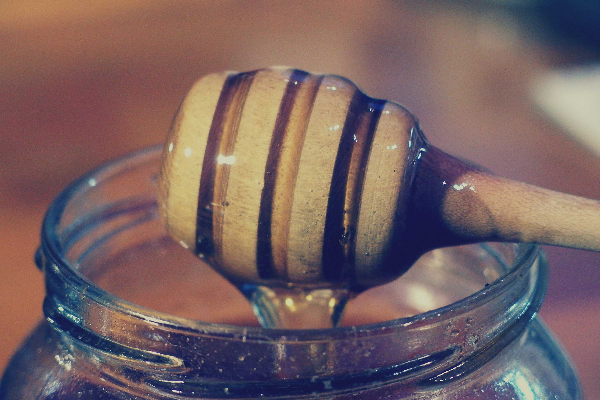 Honey on a honey stick going into a jar.