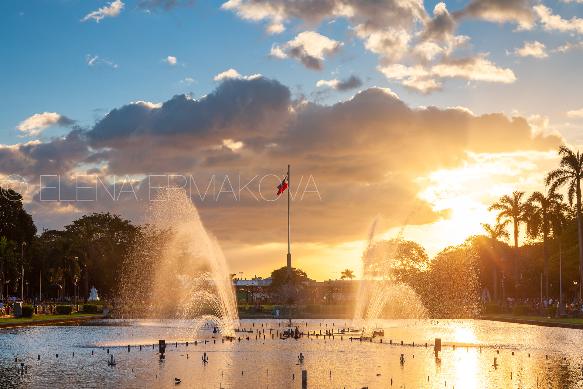 View of a fountain in Rizal Park with a flag of the Philippines under beautiful sunset light, Manila, Philippines.