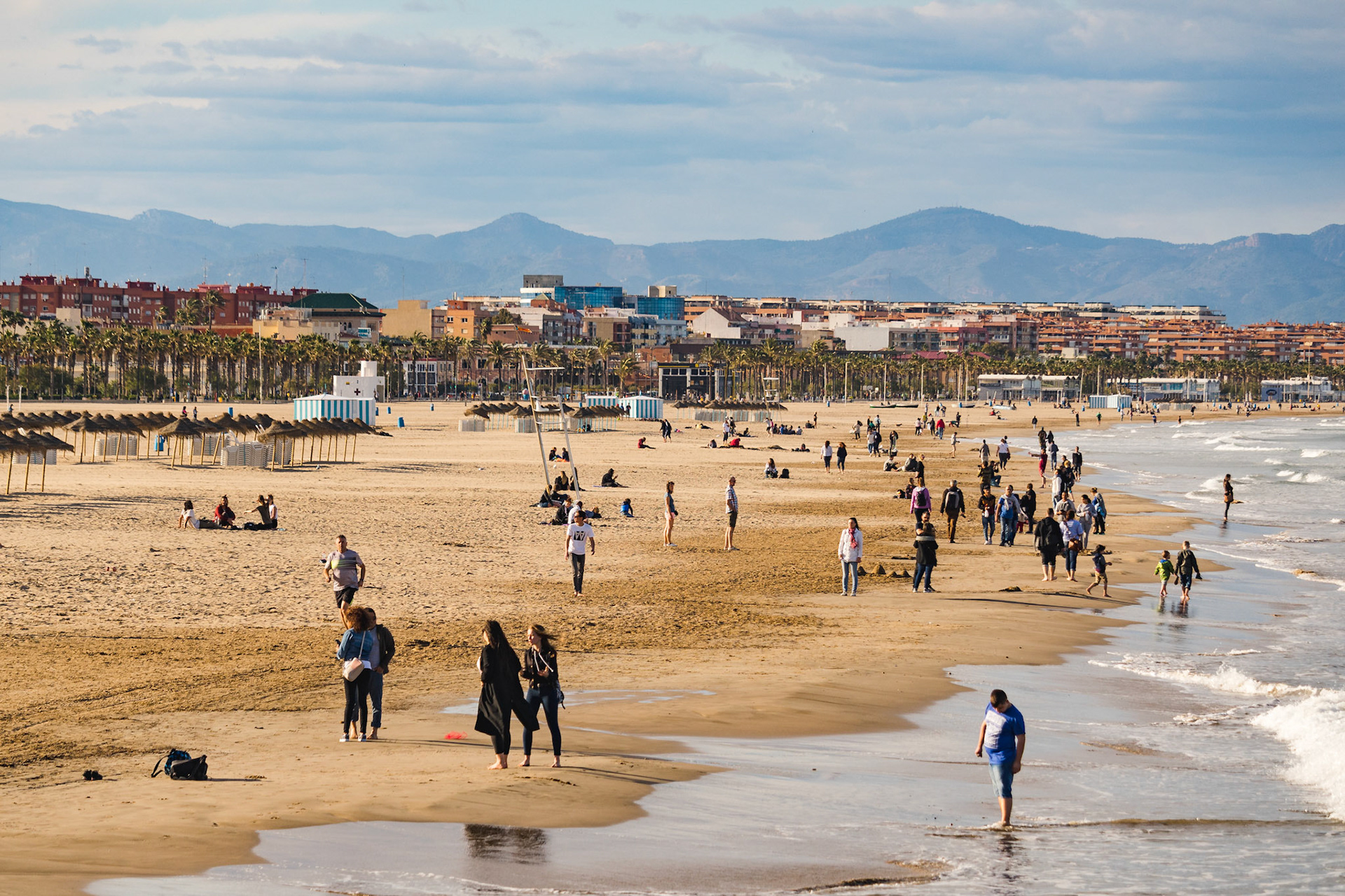 Sunny and cloudy day on La Malvarrosa beach promenade in Valencia, Spain. People on the beach. Free time activity. Relaxing on the ocean.