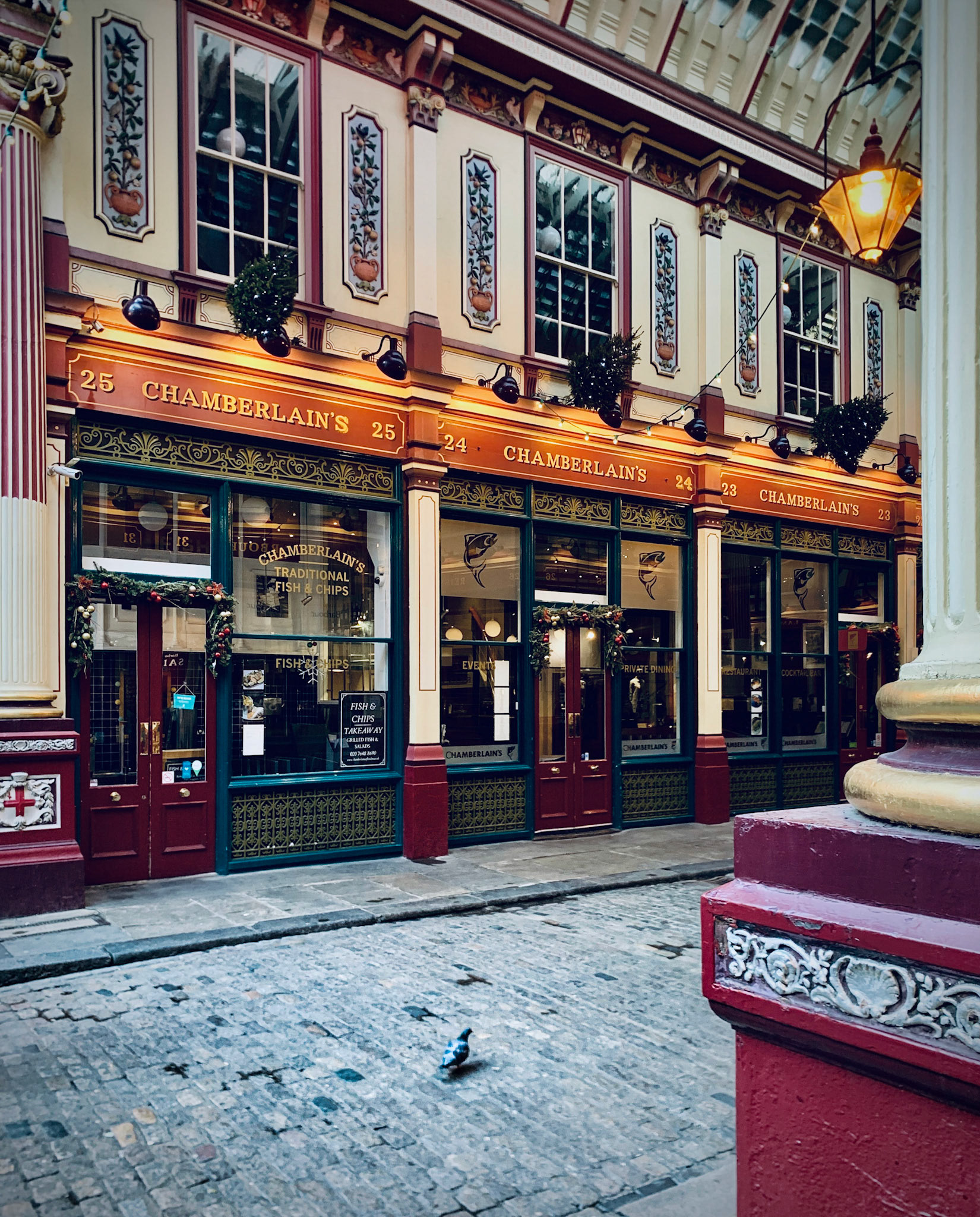 Fassaden von Ladengeschäften in historischem Ambienete. Auf dem Kopfsteinpflaster spaziert eine Taube. Leadenhall Market, Lime Street, London, Vereinigtes Königreich
