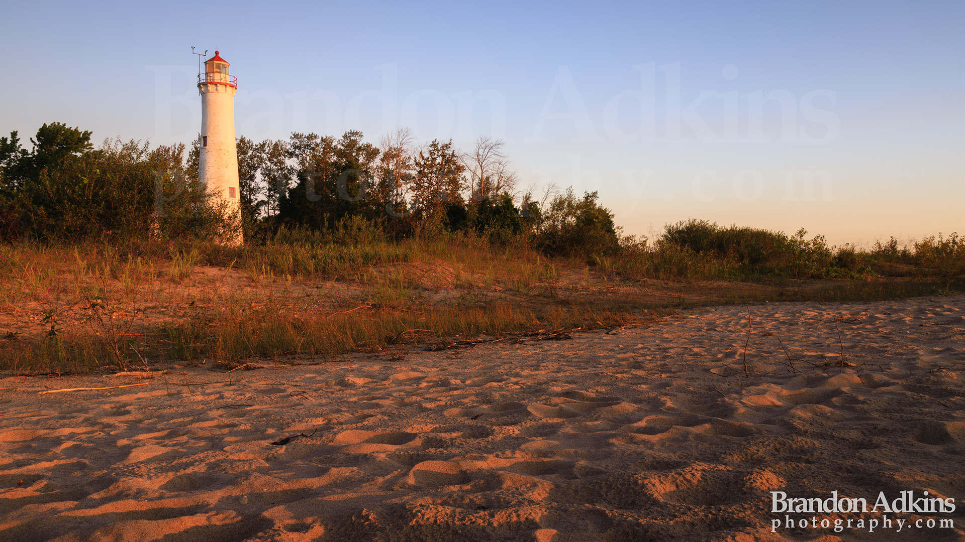 Fine art photograph of Sturgeon Point Lighthouse on Lake Huron at sunrise with light flowing over rippled sandy beach on the east coast of Michigan