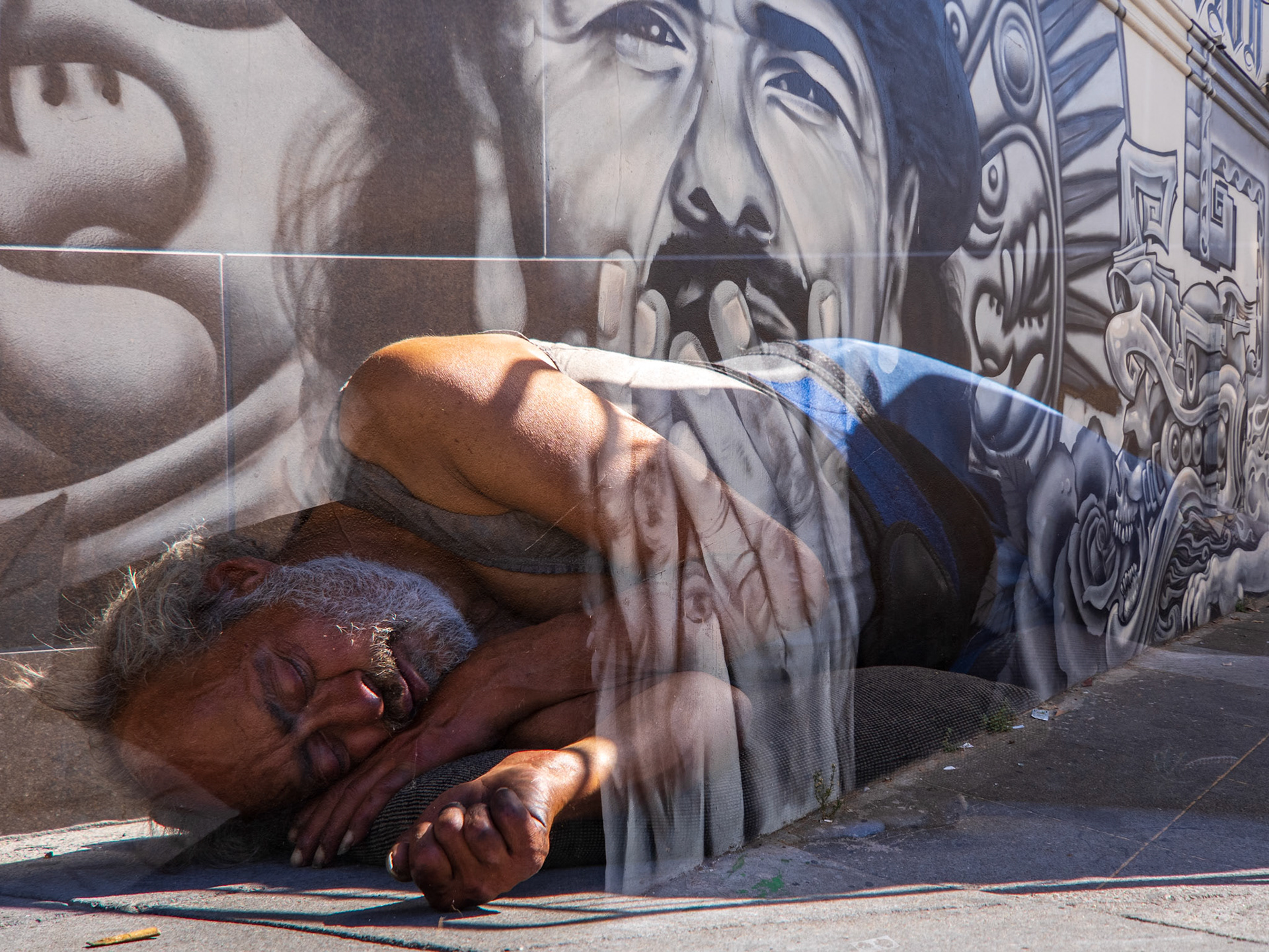 'A Veneer of Shelter', 10/15/20.  Man sleeping in the street. Mural of Santana by Mel Waters. 