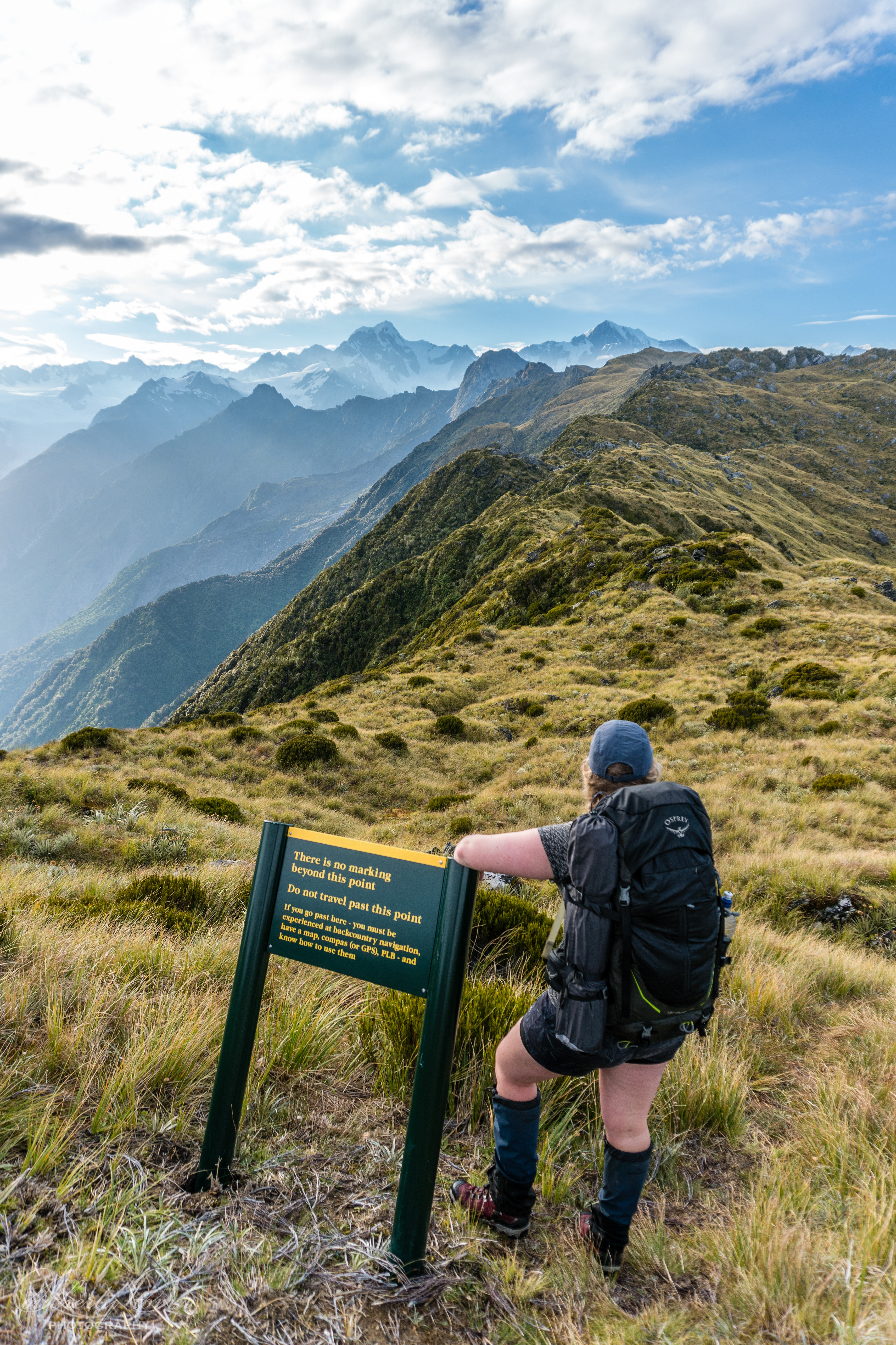 Tramper and a DoC sign observing the southern alps