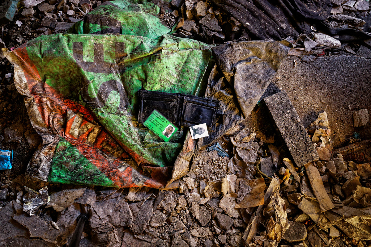 Norman The Forlkift Driver 2014 - 2016 Photographic Print UV Print, Lightbox 850mm x 850mm. The victim of a mugging's wallet lies on the ground floor of Dark City. His permit card to operate a forklift lies next to his ID photograph. The wallet has clearly been sorted through and abandoned in an eerily reflective manner of its former owner. This image speaks about crime in Dark City.