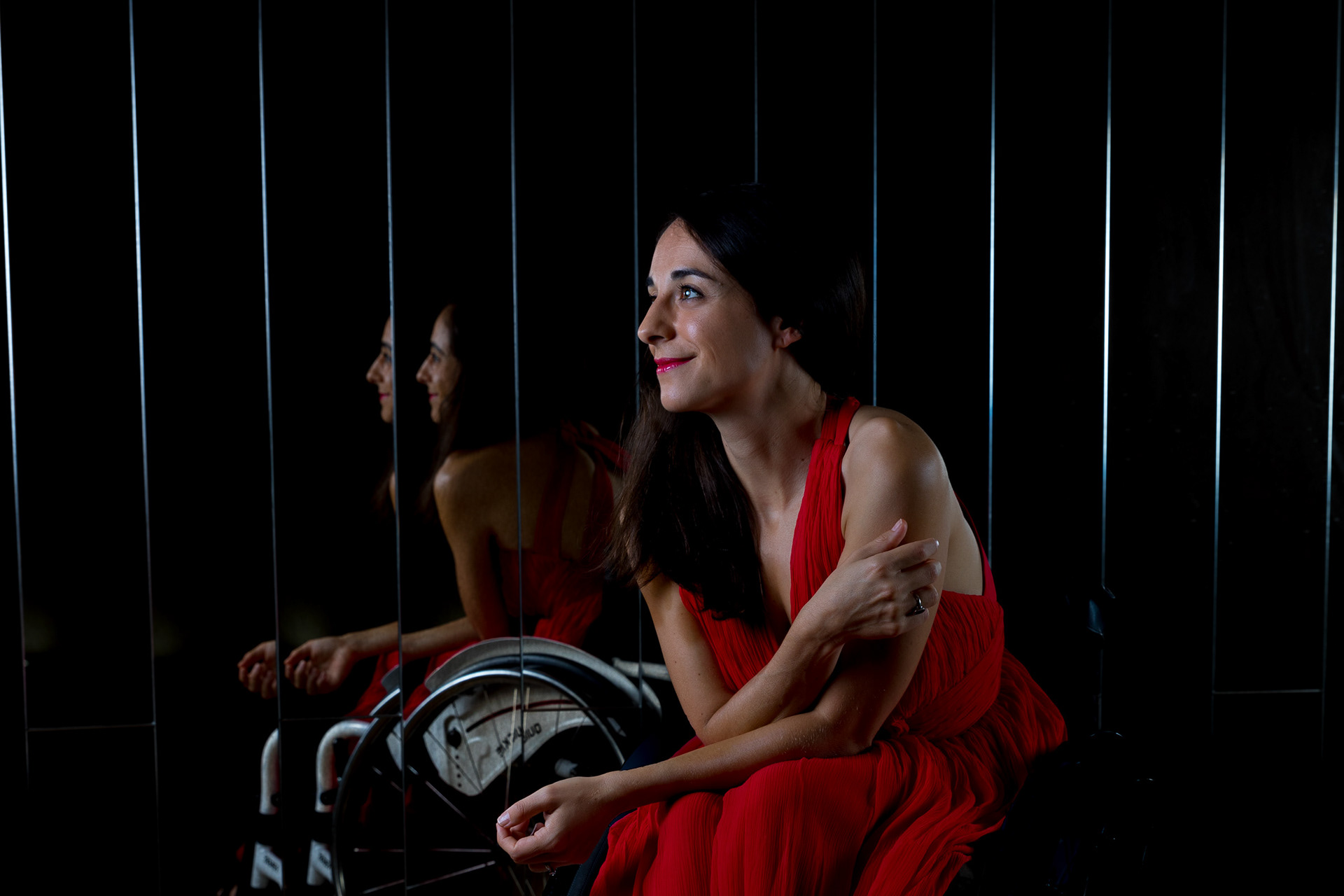 Evianne sits in front of a beveled mirror in a red dress wearing red lipstick