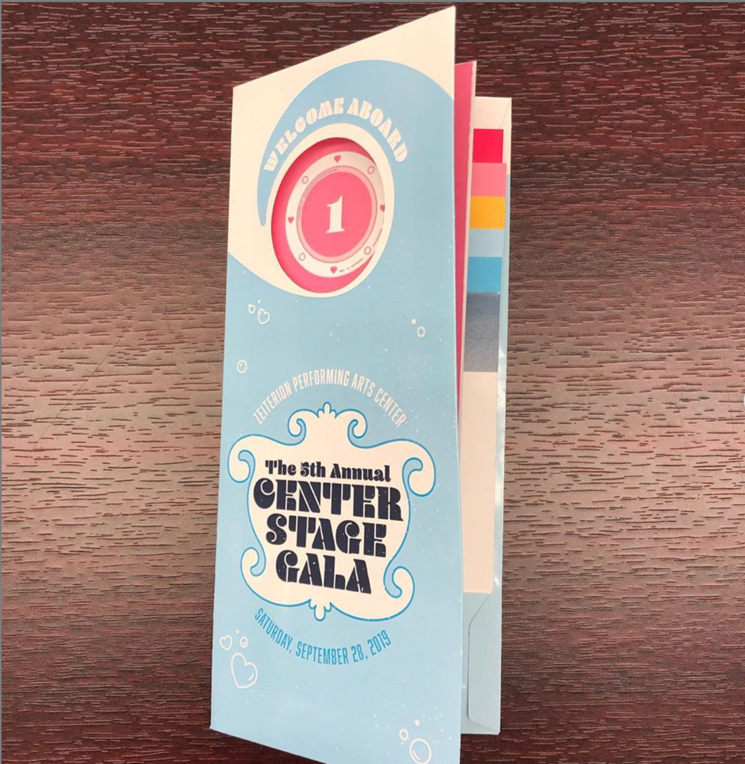 The Center Stage Gala's Itinerary. It contains a card with the guest’s table number, a timeline of the evening, the gala’s menu, and a set of donation cards. (1/7)