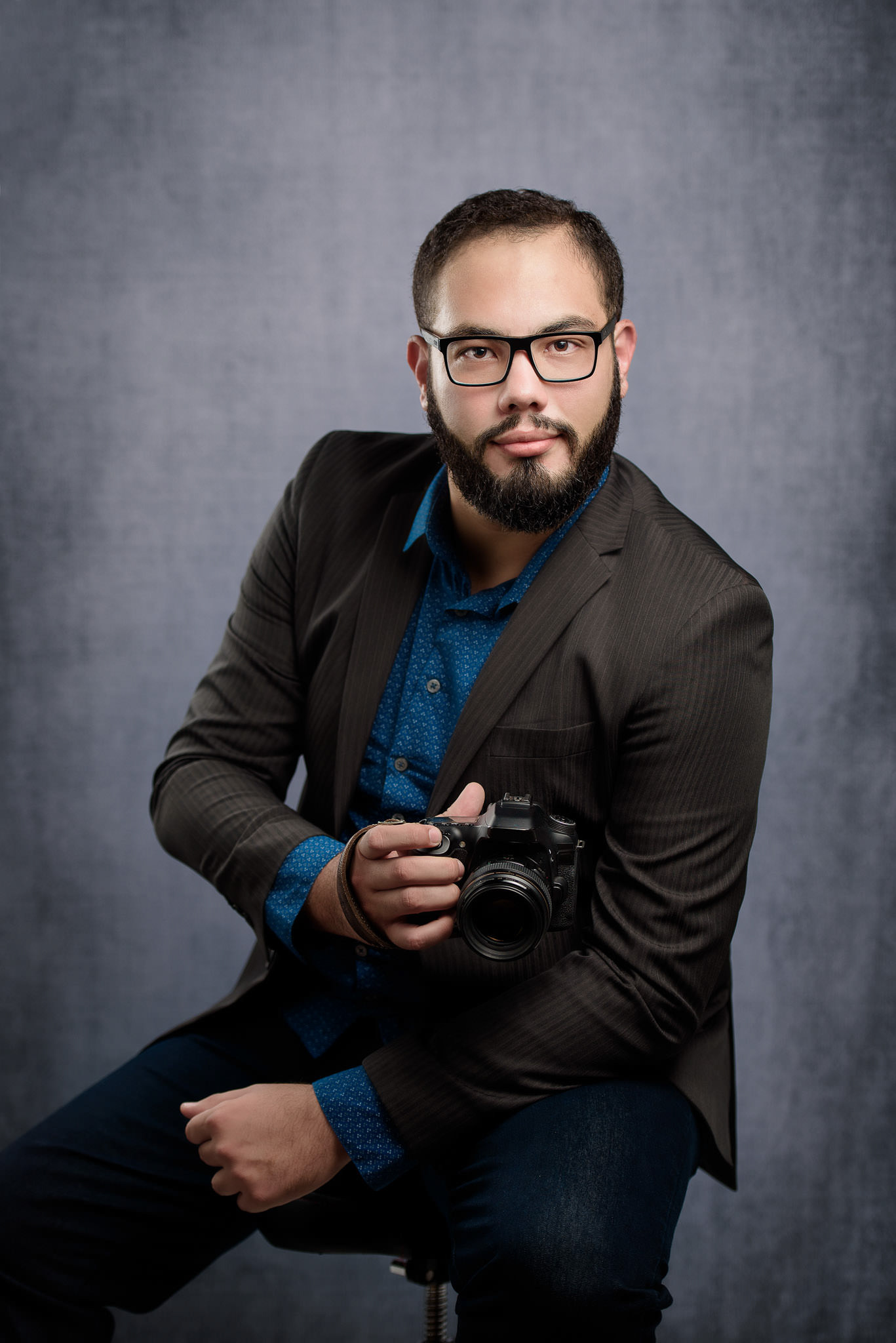 retrato de Alberth sentado, usando terno e com uma câmera fotográfica na mão