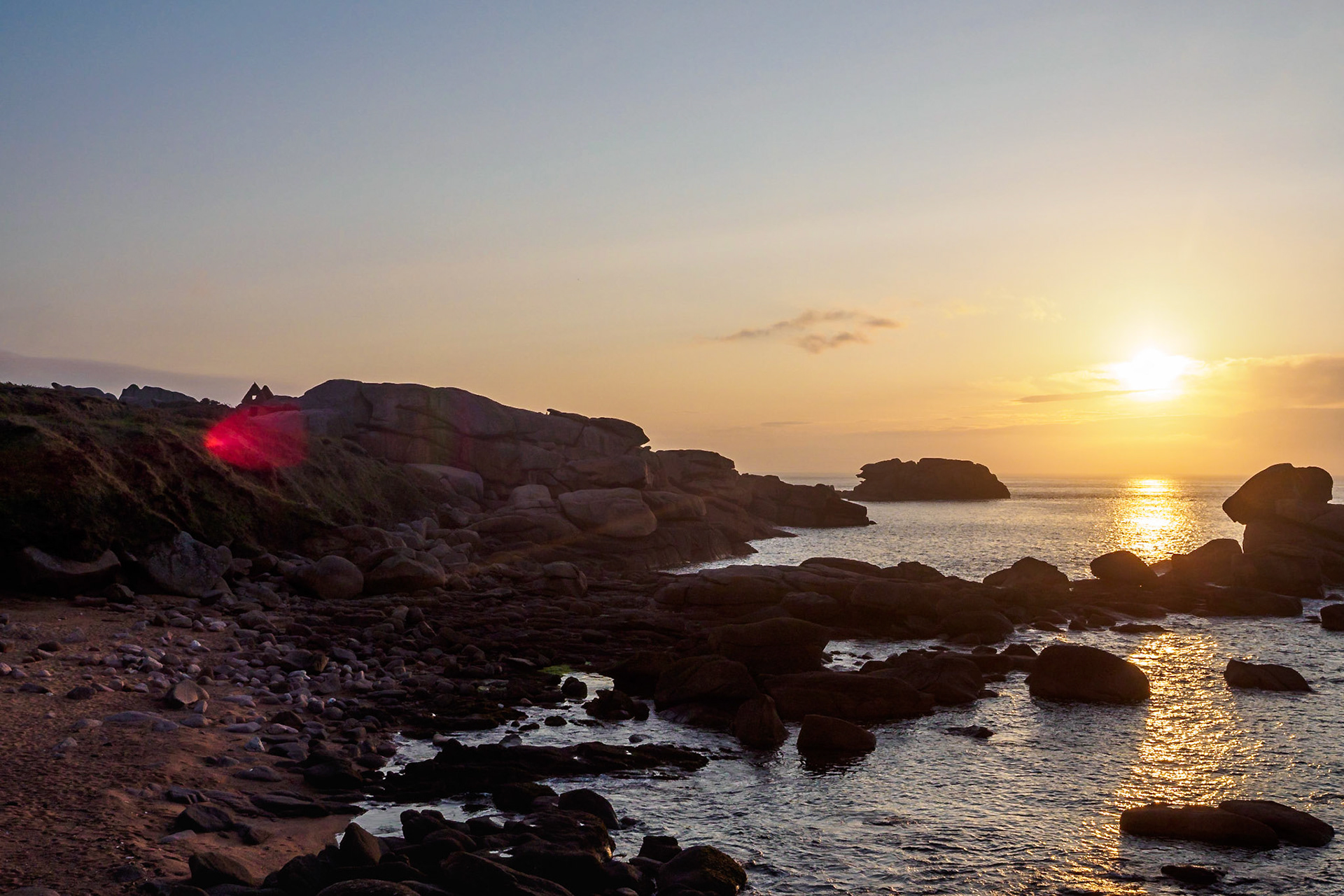 Strong lens flare  from the sun setting over the English Channel at Ploumanach, France, right under the remains of a house. the sun reflects in the water and casts a soft light over the pink granite rocks.
