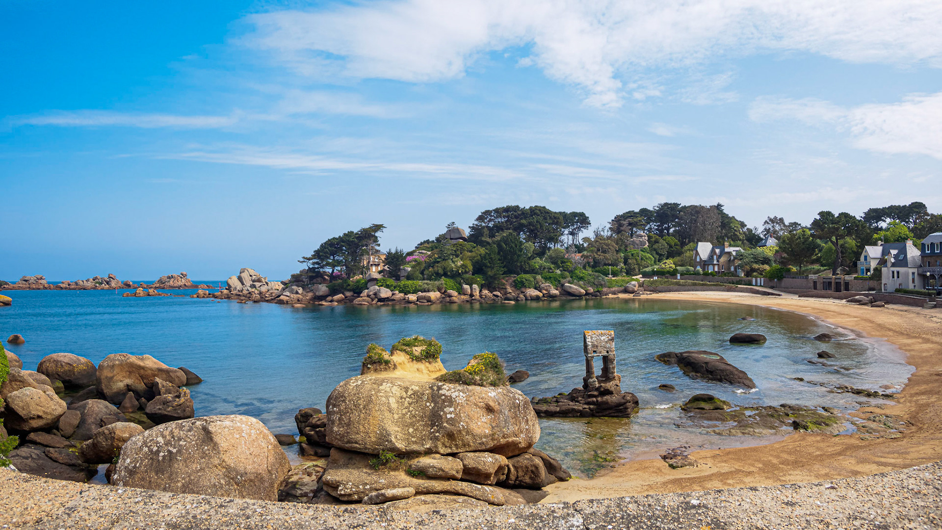 Wide-angle panorama of the bay of Saint-Guirec in Bretagne France. Juxtaposition of human elements and the rough nature under a blue though slightly clouded sky.