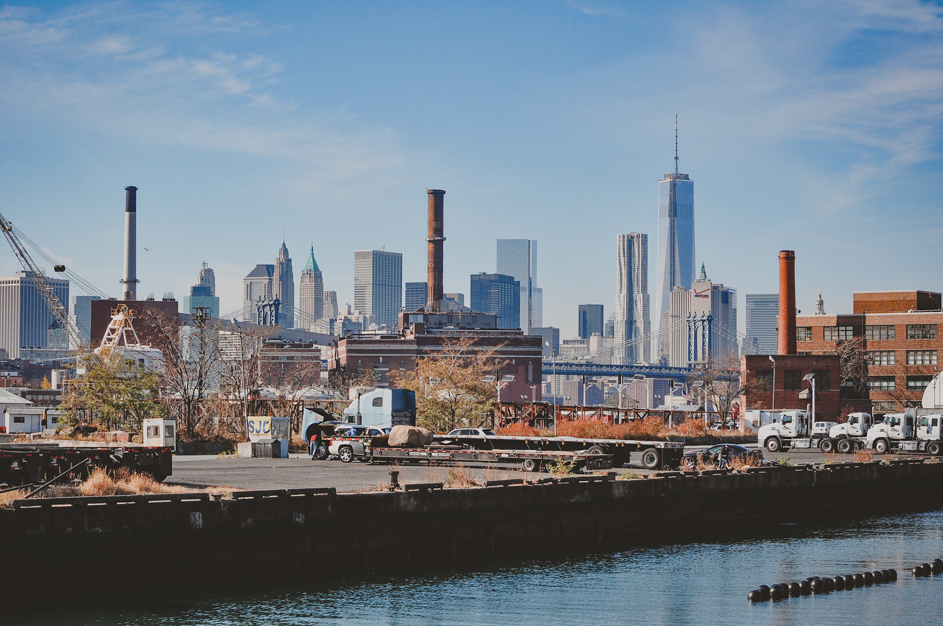 The trucks and buildings in the foreground are part of the Brooklyn Navy Yard.  The Manhattan Bridge is in the middle and the New York City skyline is in the background.