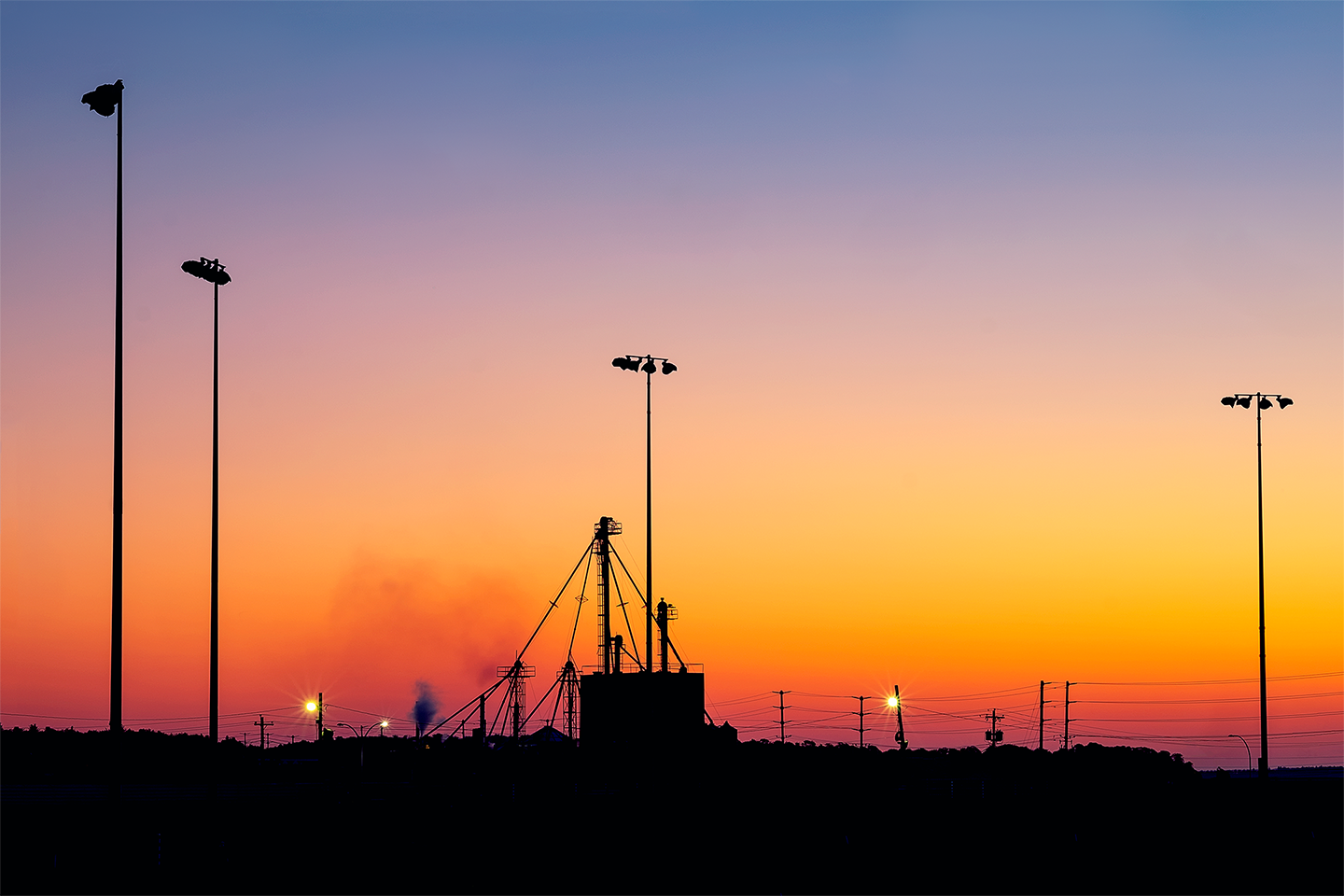Racetrack lights of varying heights tower over the grain silo in a colourful early morning sky